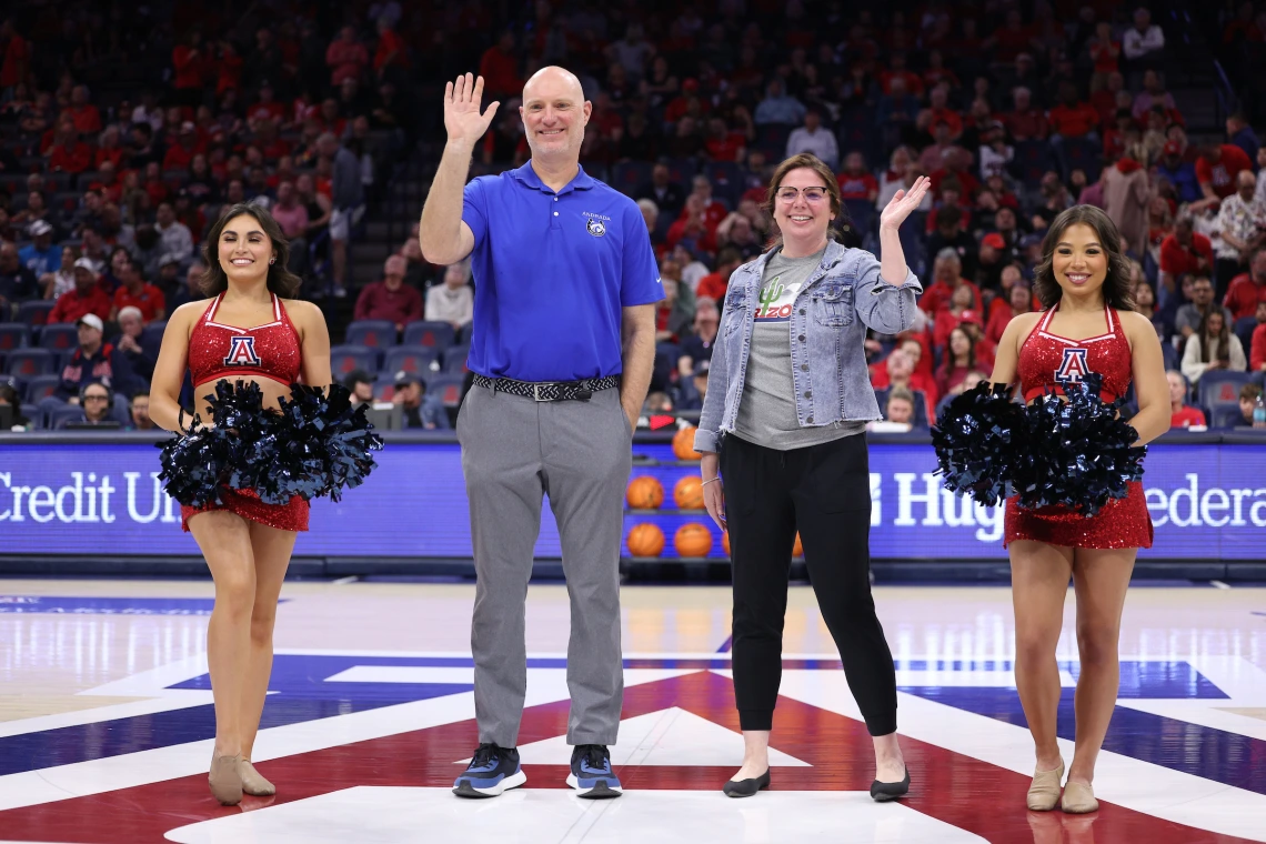 four people stand and wave from a basketball court.
